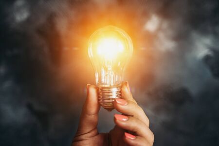 Idea and Innovation concept. Lamp or Light Bulb in Female Hand as Symbol of Inspiration on dark backgroundの写真素材