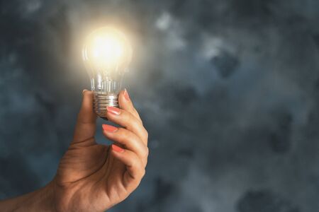 Idea and Innovation concept. Lamp or Light Bulb in Female Hand as Symbol of Inspiration on dark background with copy space from leftの写真素材