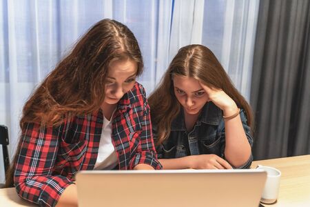 Two attractive young women at home with laptop, talking with each other and laughing. Friendship or female couple concept.の写真素材