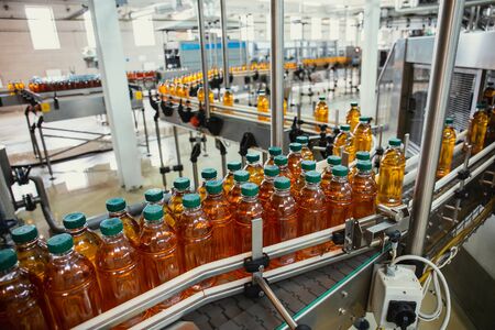 Conveyor line with plastic bottles of juice at modern factory equipment. Beverage manufacturing plant interior inside.の写真素材