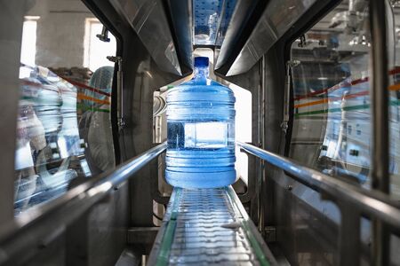 Water factory. Plastic bottle or gallon with pure water inside automated conveyor line machine.の写真素材