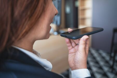 Young smiling business woman using vocal or voice activated digital assistant in smartphone, close...