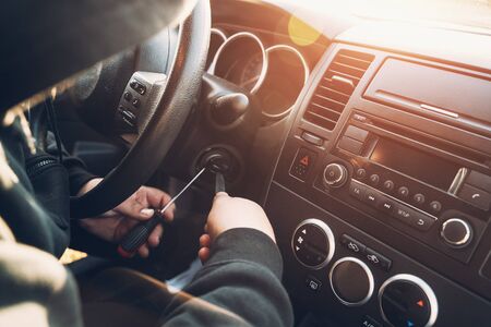 Criminal in hood trying to break and start car, car theft concept, toned