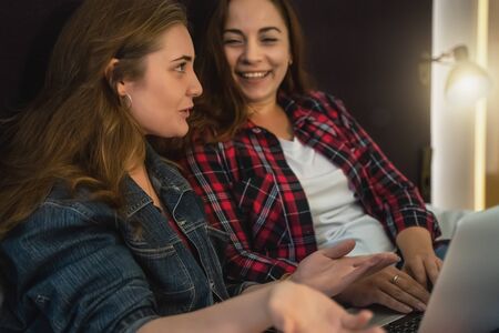 Two attractive young women talking and smiling in bed at home with laptop, toned