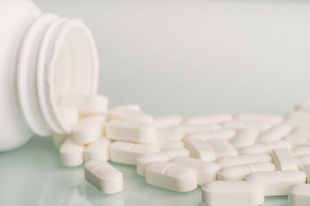 White medicine tablets spilled on table from pill bottle. Medications drugs or supplements or opioid...