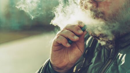 Man smokes new Vape Pod System, exhales vapor of electronic cigarette, vaping concept, selective focus, copy space.の写真素材