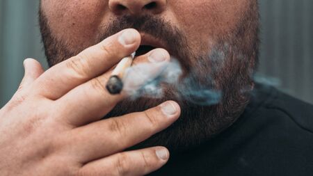 Man smoking real rolled marijuana or cannabis or weed joint tobacco cigarette, close up.