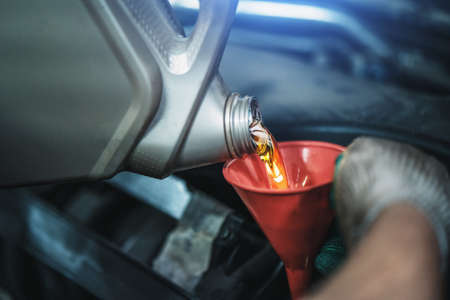 Worker pours new synthetic motor oil from canister into funnel at car service, regular oil change - auto health concept.の写真素材
