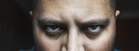 Evil look of angry or tired male with bags or black circles under spooky eyes, close up portrait. Horror creepy demon or bad negative person looks at camera.の写真素材
