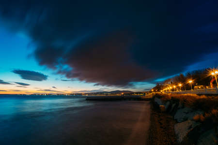 Evening on sea resort after sunset, colorful cloudy sky above sea waves and coastline in twilight.