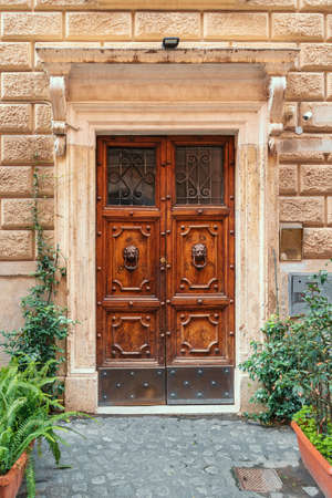 Ancient beautiful wooden door with door knockers and porch decorated with flowers in Italy, Rome.の写真素材