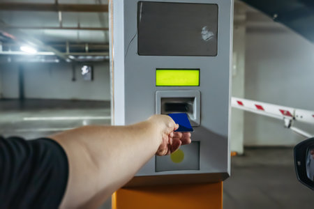 Man in car leaves underground parking in mall by paying with card near exit gate.