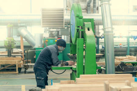 Worker at grinding machine for processing wood in workshop of woodworking plant.