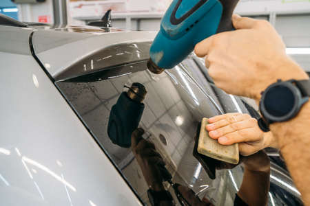 Professional detailer warms up tint film with industrial dryer to apply tinting on car glass, close up.の写真素材