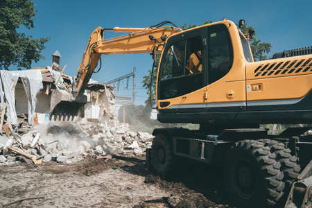 Destruction of old house by excavator. Bucket of excavator breaks concrete structure.