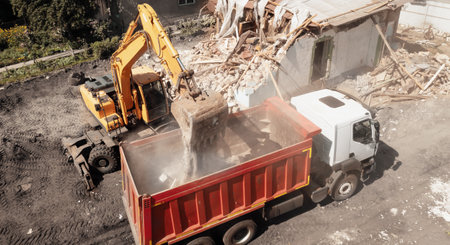 Excavator bucket loads industrial debris into truck. Process of demolishing and destruction old house. Release of quarters for new development.の写真素材