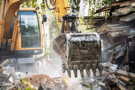 Excavator bucket breaks old house. Building demolition. Structure dismantling.