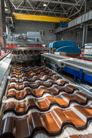 Brown metal roof tiles made from galvanized and painted steel in metal sheet forming machine in metalwork factory.の写真素材