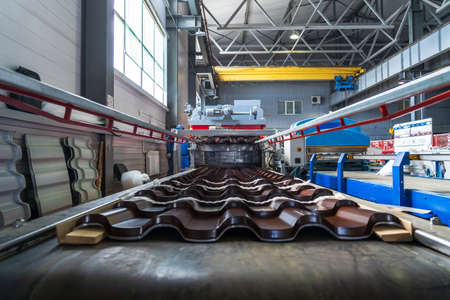 Brown metal roof tiles made from galvanized and painted steel in metal sheet forming machine in metalwork factory.の写真素材