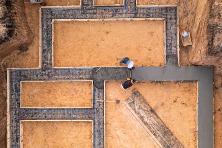 Workers leveling poured liquid concrete or cement on steel reinforcement, building foundation construction in process, aerial top view.の写真素材