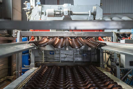 Metal tile for roof in metal forming machine production line close up. Industrial background.