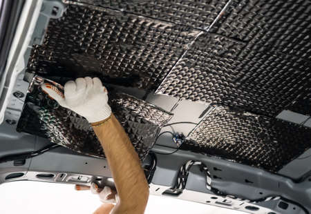 Worker hands glues soundproofing material to inside of car roof. Process of car sound insulation...