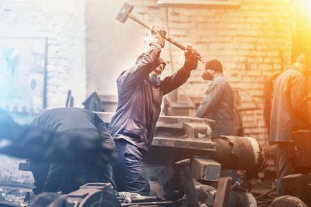 Worker swings large hammer in workshop of metallurgical plant.の写真素材