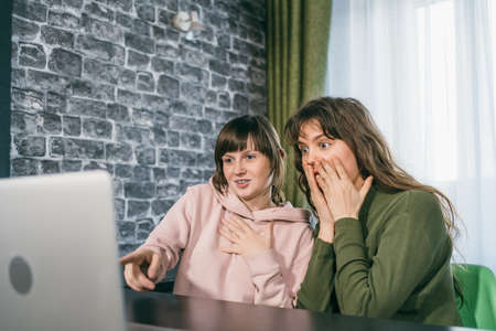 Two young women receive good news by internet or winning lottery looking at laptop. Happy surprised girl gets positive emotion.の写真素材