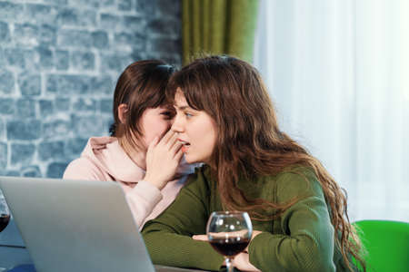 Young cute woman whispering secret on ear to her female friend. Communication and surprised girl by gossip.の写真素材