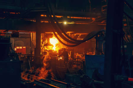 Iron casting process in metallurgical factory. molten metal pouring from ladle in workshop.