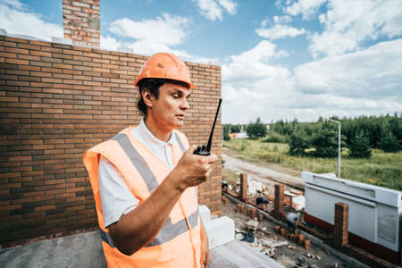 Foreman inspector or construction worker in hardhat portrait. Engineer in helmet with walkie-talkie in hand directs construction process.の写真素材