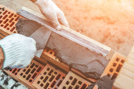 Worker or bricklayer works with trowel laying bricks. Builder makes brickwork on construction site, close up on hands.の写真素材