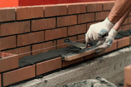Mason trowels smears cement mortar on brick. Bricklaying when building house or stone fence.の写真素材