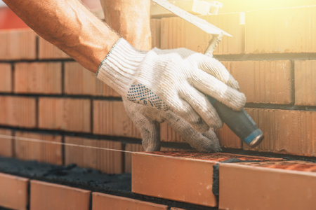 Bricklayer taps with trowel on newly laid brick on cement mortar. Brick wall construction.