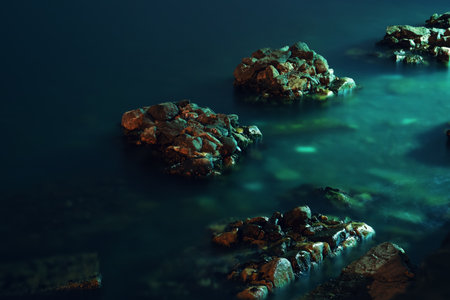 Dark dramatic Rock stones in blue green sea water at night long exposure.の写真素材