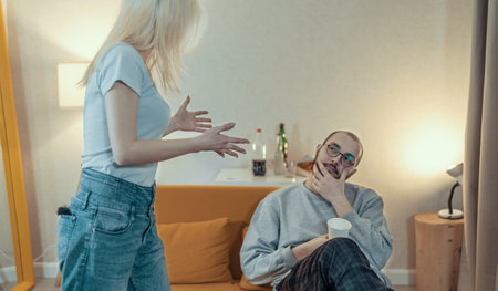 Young couple is arguing, girl screaming and scolding her husband, sitting on couch. Man was guilty, problems in relationships and difficulties in understanding.の写真素材