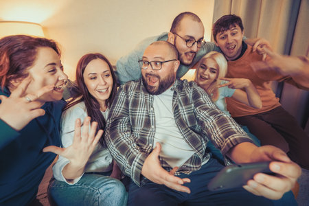 Group of young people taking selfie on smartphone at home party and have fun. Friends enjoy their company, smiling.の写真素材