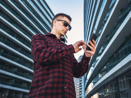 Young businessman student worker using mobile phone in hands at modern new blue office building towers.の写真素材