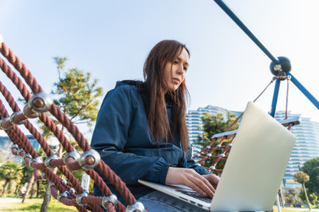Portrait of young beautiful freelancer woman sitting in hammock in park and working at laptop.の写真素材