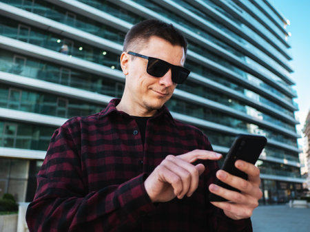 Young man in sunglasses using mobile phone in hands at modern new office building background.の写真素材