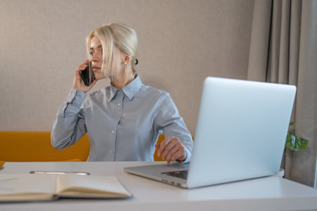 Young girl office worker or business lady is talking on phone and working on laptop.の写真素材