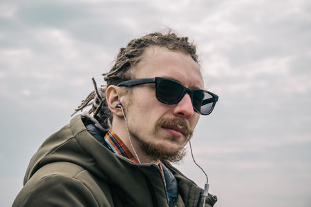 Portrait of cheerful guy with glasses and dreadlocks in-ear headphones or earphones listen to music....
