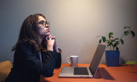 Serious young woman in glasses sit at laptop and thinking. Tired and stressed freelancer at home...