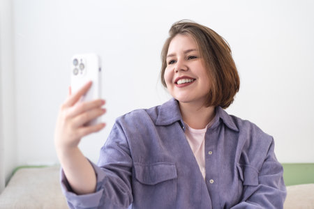 Plus size smiling young woman taking selfie with mobile phone.の写真素材