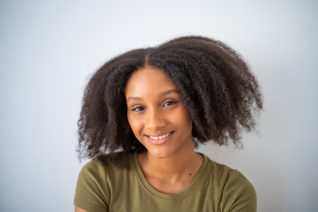 Cute African American girl with Afro hairstyle smiling and looks at camera. Portrait of female black positive teenager.の写真素材