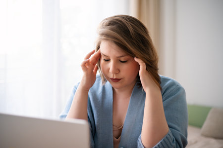 Plus size young woman massaging temples by fingers, headache and health problems, impact of stress on life and appearance of depression, anxiety disorders.の写真素材