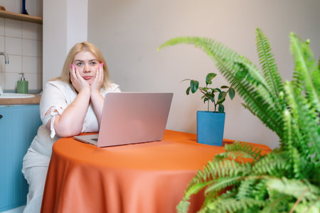 Tired overworked plus size woman sitting in stress or depression at table with laptop. Bored person alone.の写真素材