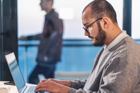Young businessman working on laptop in office. Portrait of IT software engineer in glasses, side...