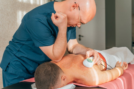 Portrait of male massage rehabilitation therapist doing elbow massage on patient back.の写真素材