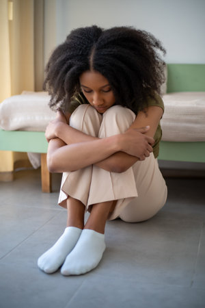 Young African American girl sits with hands on knees. Stress emotion, vertical image.の写真素材